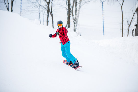 Image of sportive snowboarder man riding on snowy hill