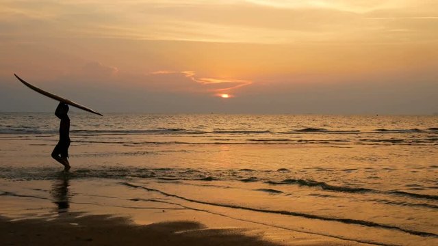 silhouette of young happy surf man running with long surf boards at sunset on tropical beach. surfer on the beach in sea shore at sunset time with beautiful light. surfing for water sport activity