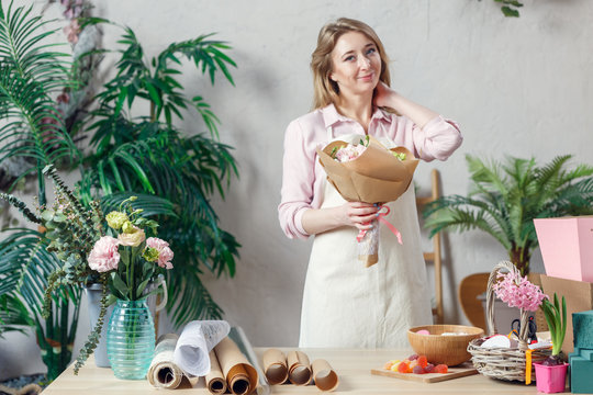 Image of smiling florist in apron with bouquet of flowers with kraft paper