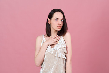 Obraz premium an attractive girl with a surprised expression puts her palm on her chest and looks carefully at the camera. 