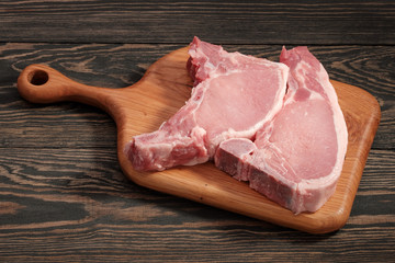 Two pieces of raw fillet of pork loin on a wooden board on a dark wooden table