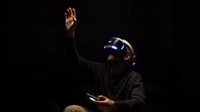 Portrait of game boy 20s immersing in cyberspace while playing video simulation in virtual reality, using digital glasses and controller in dark room