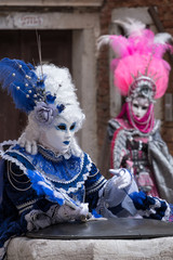 Fototapeta na wymiar Women in costume with fans and ornate painted feathered masks at Venice Carnival. 