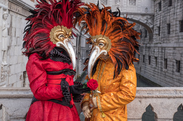 Pair of costumed and masked carnival-goers standing in front of the Bridge of Sighs during Venice...