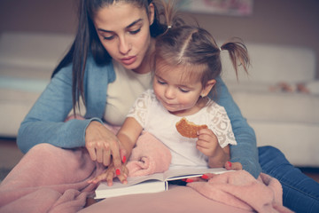 Mother and daughter reading book together at home.