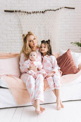 Portrait of mother with two daughters in the white room in the same pink pajamas, family look