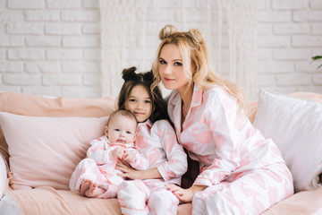 Fototapeta na wymiar Portrait of mother with two daughters in the white room in the same pink pajamas, family look