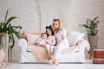 Obraz premium Portrait of mother with two daughters in the white room in the same pink pajamas, family look