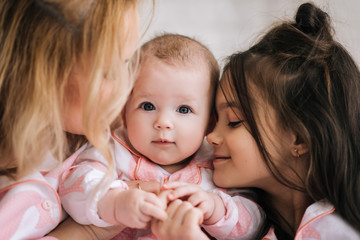 Portrait of mother with two daughters in the white room in the same pink pajamas, family look