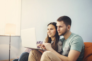Fototapeta premium Young couple sitting at home and using laptop, surf the Internet.