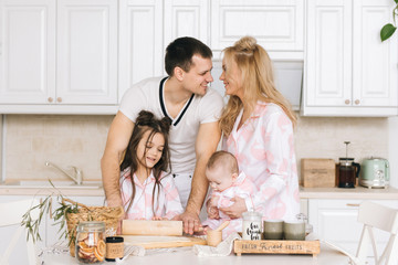 Obraz na płótnie Canvas Happy loving family are preparing bakery together. Mother father and two daughter girl are cooking cookies and having fun in the kitchen. Homemade food and little helper.