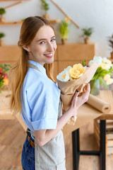 young female florist holding beautiful bouquet of tulips and smiling at camera in flower shop