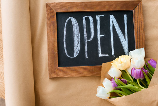 top view of beautiful tulips and open sign on craft paper