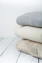 Knitted wool sweaters. Pile of knitted winter clothes on wooden background, sweaters, knitwear, space for text.