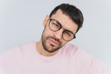 Closeup self portrait of serious macho man wears trendy round glasses and pink clothes posing isolated over white background in studio wall. People, lifestyle and emotion concept.