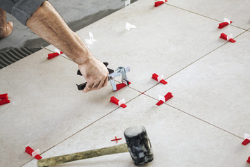 Ceramic Tiles. Tiler placing ceramic wall tile in position over adhesive with lash tile leveling...