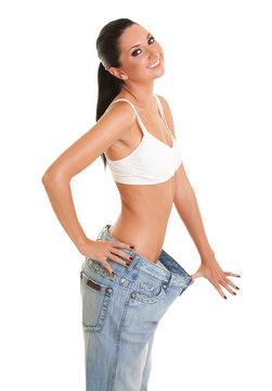 Happy smiling woman shows her weight loss by wearing an old jeans, isolated on white background. Close up of sporty and beautiful woman. Healthy lifestyle, dieting, fitness, weight loss concept