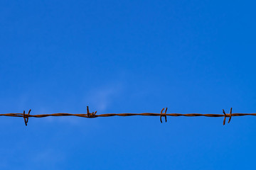 Rusty barbed wire fence against clear blue sky with copy space
