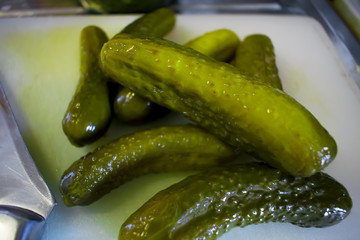 Several salted small salted cucumbers on a white cutting board, next to a knife.