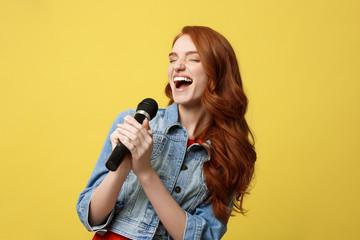 Lifestyle and People Concept: Expressive girl singing with a microphone, isolated bright yellow background.