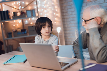 Grandfather and grandson are watching video at night at home.