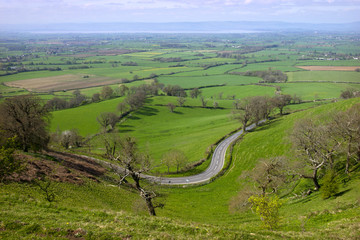Fototapeta na wymiar Panoramic view towards the River Severn over a patchwork of fields with a winding road in the foreground, Coaley Peak viewpoint, Gloucestershire, UK