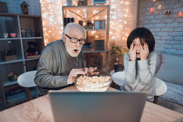 Grandfather and grandson are watching scary movie at night at home.