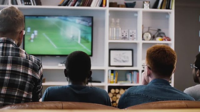Four African American guys watch football on TV. Back view. Excited fans on the couch together. Emotion. Bonding time.