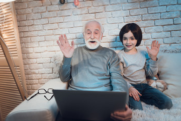 Grandfather and grandson are talking on skype with family at night at home.