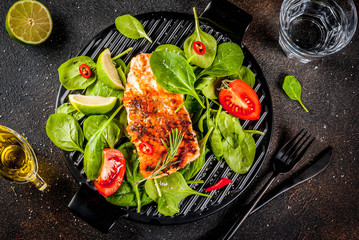 Grilled salmon steak filet with fresh vegetables, spinach and lime, dark rusty table copy space top view