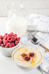 Healthy breakfast, semolina porridge with milk and raspberry, white marble table copy space