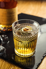 Glass of  whiskey (cognac or brandy) with lemon and ice cubes standing on the bar counter with a bottle on the background