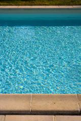 Fototapeta na wymiar Stone edging detail beside a blue swimming pool sunshine surface ripples.