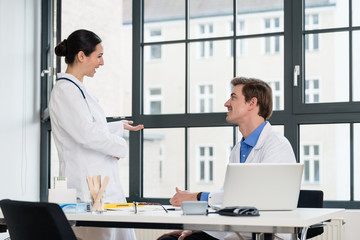 Young female physician using a tablet PC while asking for advice from her experienced male colleague in the office a modern hospital