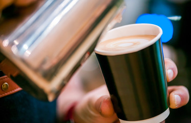 Barista pouring steamed milk into takeaway coffee cup, cropped