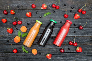 Naklejka na ściany i meble Three bottles of juice and fruits on black wooden background. Food concept