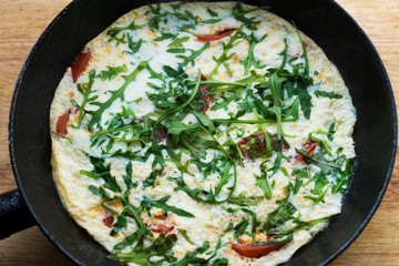 freshly cooked omelette with tomatoes and arugula hot in a pan