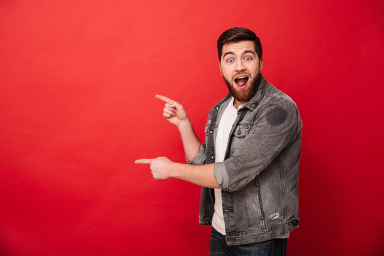 Photo of excited man 30s in casual clothing gesturing fingers aside on copyspace with surprise, isolated over red background