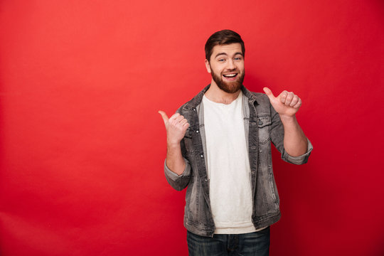 Photo of handsome man 30s in casual clothing gesturing fingers aside on copyspace with surprise and smile, isolated over red background