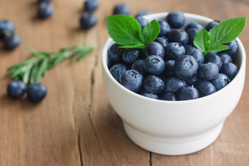 Fresh blueberries heap in white bowl in side view with copy space on wood table for background in vintage tones. Blueberry is healthy and delicious fruits which have high antioxidant and vitamin C.