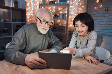 Grandfather and grandson are watching movie on tablet at night at home.