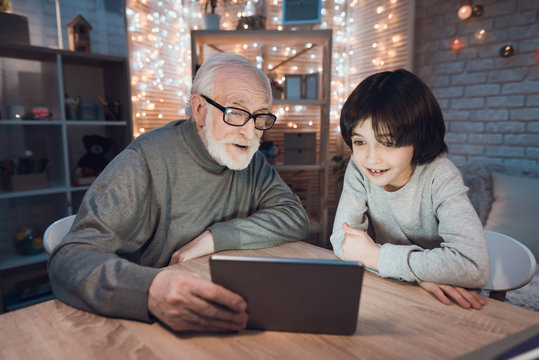 Grandfather and grandson are watching movie on tablet at night at home.