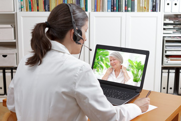 Doctor with headset and laptop, taking notes during a video call with a patient suffering from...