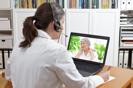 Doctor with headset and laptop, taking notes during a video call with a patient suffering from shoulder pain, telehealth or telemedicine concept.