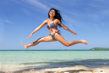 A happy cheerful girl in the bikini jumping to the height on the sea beach. Active holidays on the tropical island. Beautiful asian woman runs in the transparent sea.