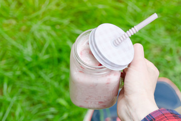 Strawberry smoothies in female hand on a background of green grass