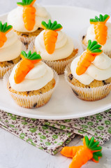 Vanilla cupcakes with chocolate chips and cream cheese frosting decorated with carrot marmalade in a plate on a white stone background.