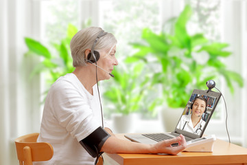 Senior woman in her living room in front of a laptop checking her blood pressure during a video call with her doctor of cardiology - obrazy, fototapety, plakaty