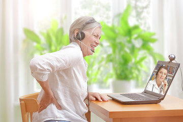 Telemedicine concept: senior woman with acute low back pain in front of a laptop during a video...