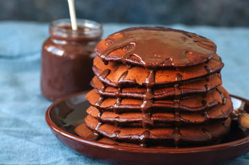 Close up of chocolate pancakes wiyh syrup in a plate on a blue background.